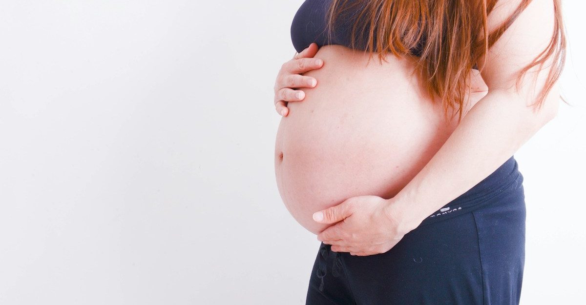 A woman clutches her pregnant belly.