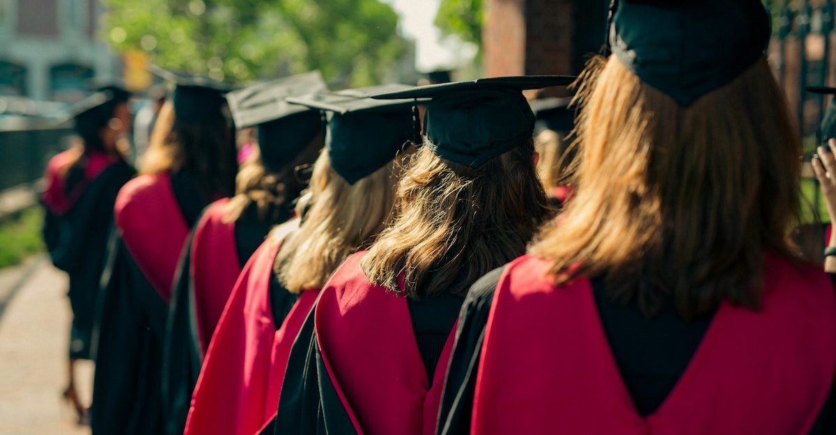 Students, potentially those attending the University of Windsor, stand in a line wearing graduation robes and caps.