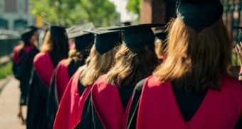 Students, potentially those attending the University of Windsor, stand in a line wearing graduation robes and caps.