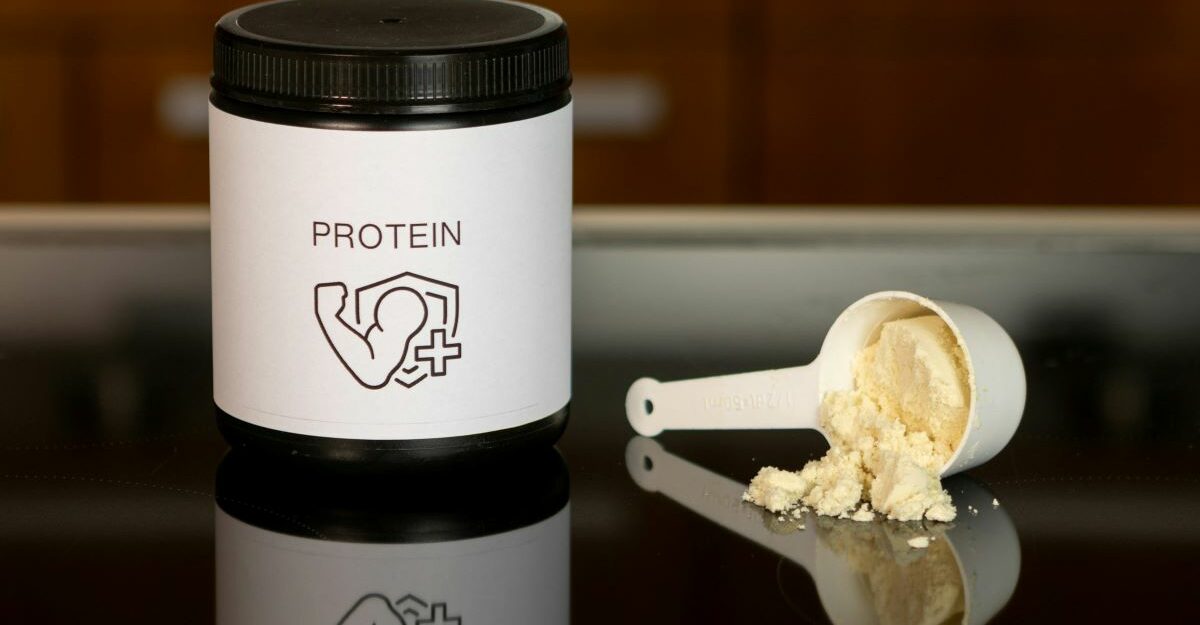 A container of protein powder, potentially made by Iovate Health, sits next to an overturned measuring cup.