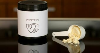 A container of protein powder, potentially made by Iovate Health, sits next to an overturned measuring cup.