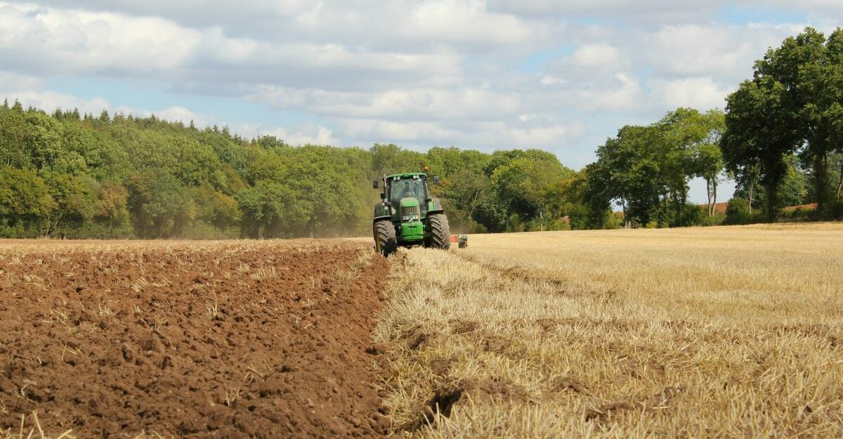 A tractor, potentially made by John Deere, works a farmer's field in Canada.