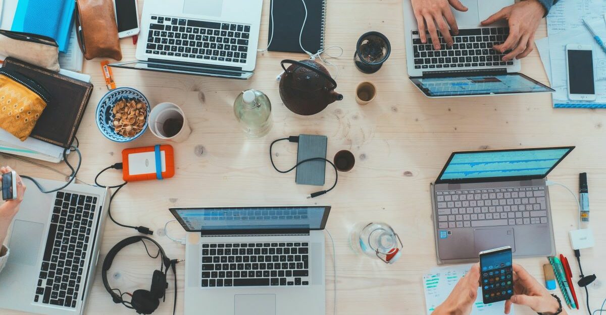 A number of work devices including laptops and smartphones clutter a table, perhaps being used by young Alberta workers.