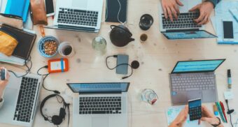 A number of work devices including laptops and smartphones clutter a table, perhaps being used by young Alberta workers.