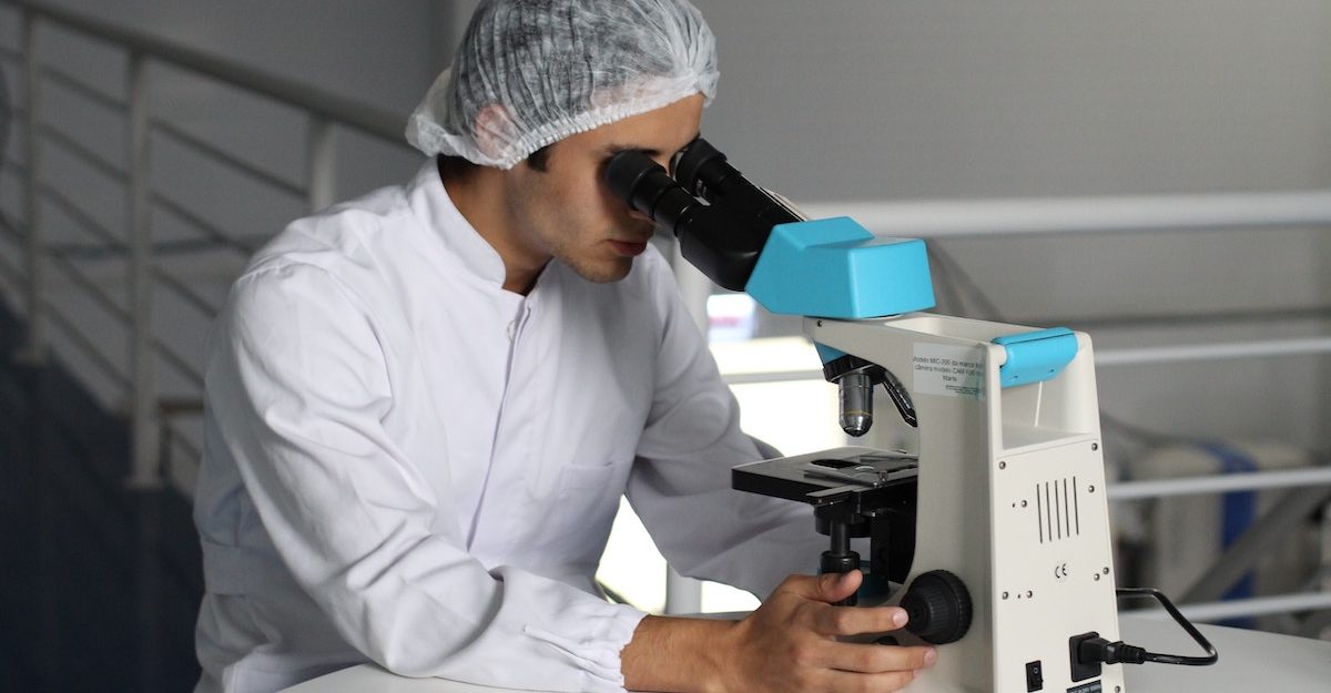 A lab technician, potentially employeed by Quest Diagnostics, looks into a microscope.