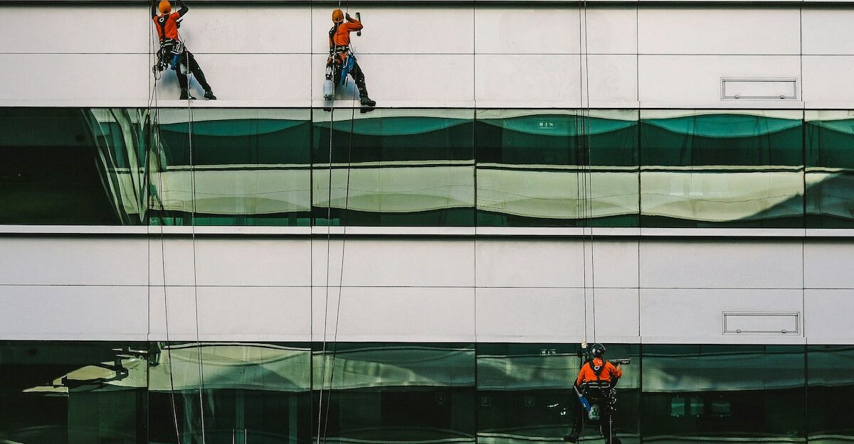 Three rope access window cleaners dangle from the side of a building as they wash.