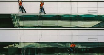 Three rope access window cleaners dangle from the side of a building as they wash.