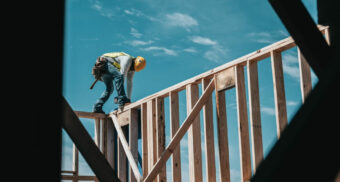 A construction worker works on top of a wooden house frame, potentially supplied by Tiaga Building Products.