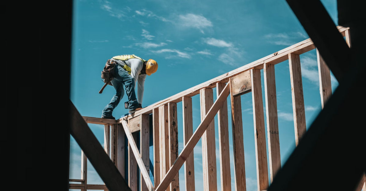 A construction worker works on top of a wooden house frame, potentially supplied by Tiaga Building Products.