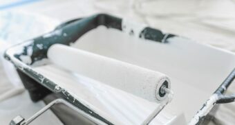 A paint roller sits on a tray which is potentially filled with Benjamin Moore paint.