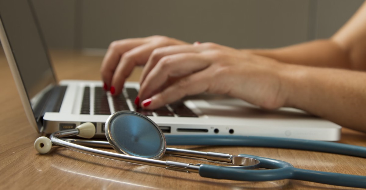 A photo of a person using a laptop with a stethoscope beside them. (Photo: National Cancer Institute / Unsplash)