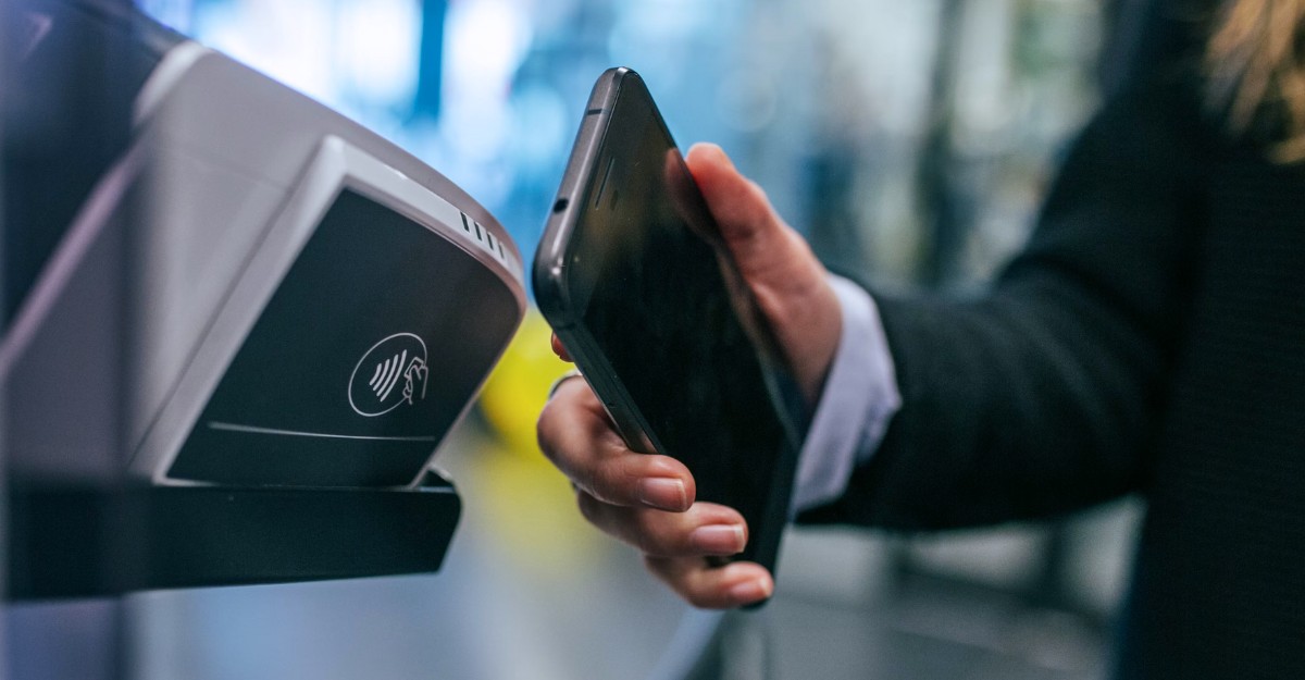 A photo of a person using an app on their phone at a contactless payment terminal. (Photo: Jonas Leupe / Unsplash)