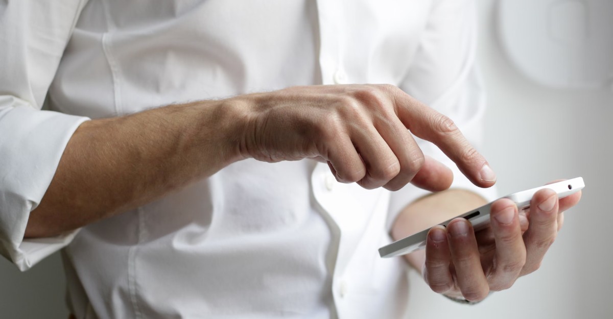 A photo of a person in a white dress shirt interacting with a phone. (Photo: NordWood Themes / Unsplash)