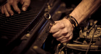 An auto worker uses tools on a vehicle's engine. (Photo: Christian Buehner / Unsplash)