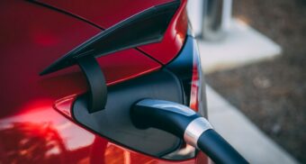 A photo of a charger inserted into a red Tesla. (Photo: Vlad Tchompalov / Unsplash)