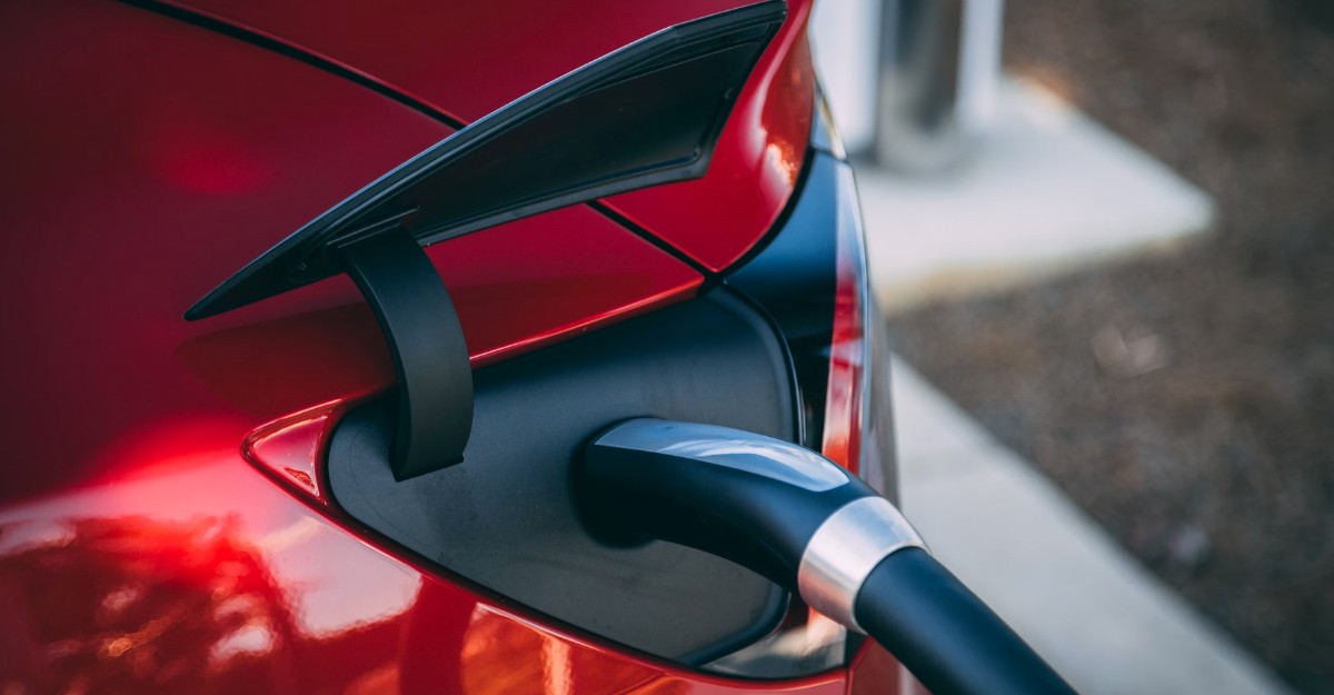 A photo of a charger inserted into a red Tesla. (Photo: Vlad Tchompalov / Unsplash)