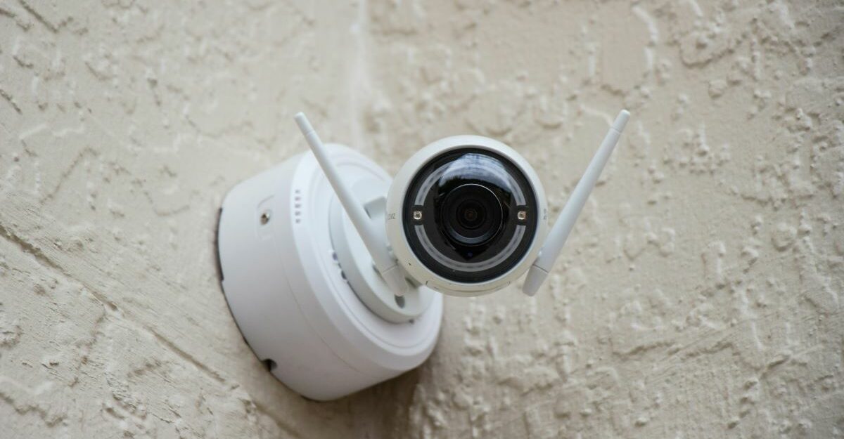 A small, white security camera sits in a corner where two walls meet.