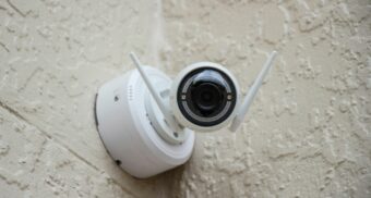 A small, white security camera sits in a corner where two walls meet.