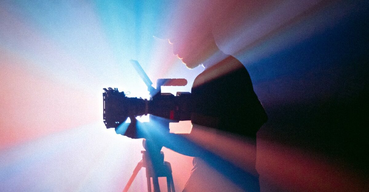 A photo of a person examining a camera in front of a projector. (Photo: Jakob Owens / Unsplash)