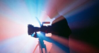 A photo of a person examining a camera in front of a projector. (Photo: Jakob Owens / Unsplash)