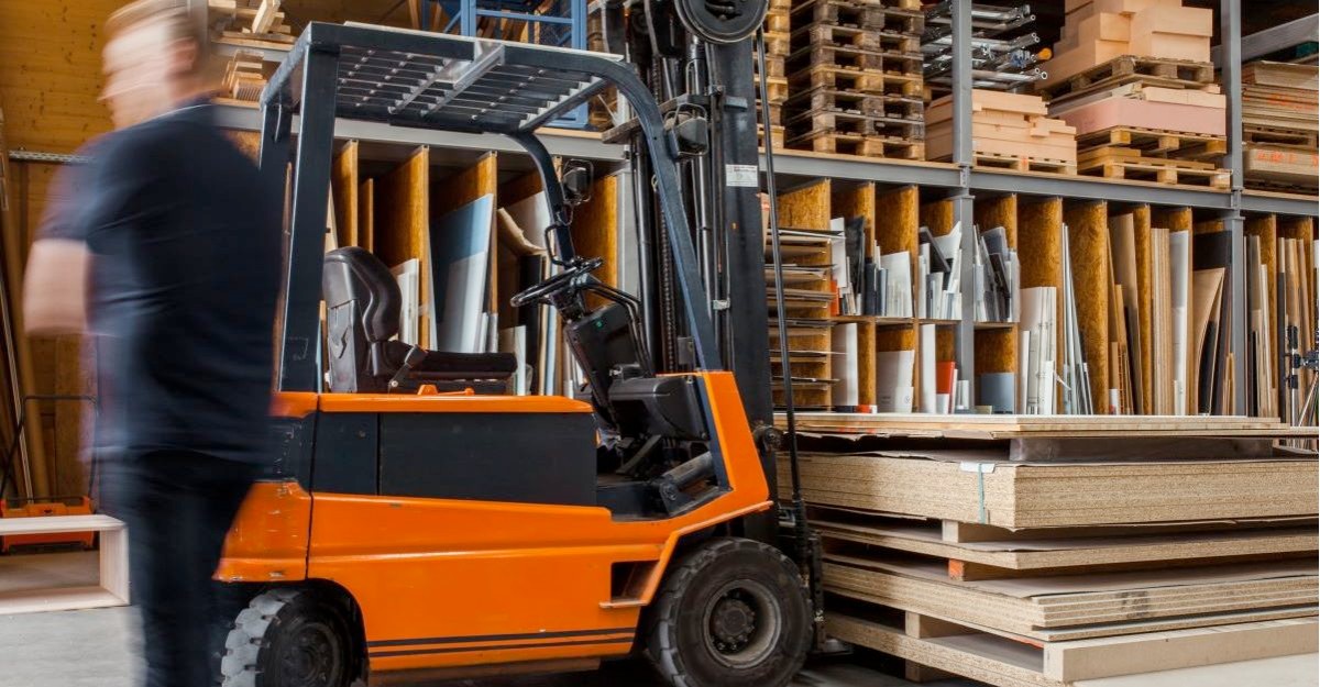 A photo of a person walking past a forklift in a warehouse (Photo: Pickawood / Unsplash)