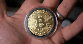 A Bitcoin sits in the palm of someone's hand.