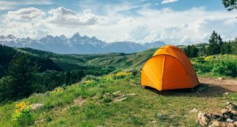 A photo of an orange tent on a hill facing a mountain range. (Photo: plasticmind / Unsplash)