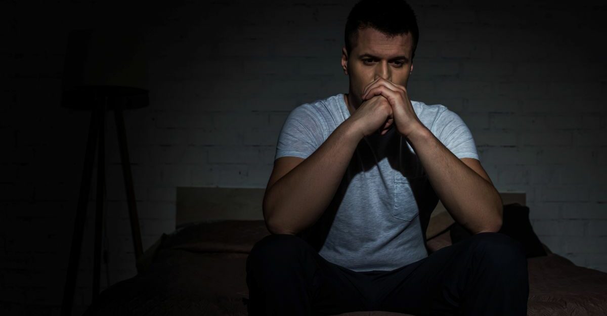 Man sitting on bed in dark room, looking distressed and deep in thought, symbolizing PTSD after a car accident in Ontario.