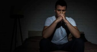 Man sitting on bed in dark room, looking distressed and deep in thought, symbolizing PTSD after a car accident in Ontario.