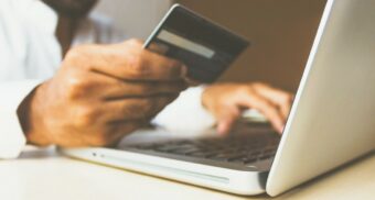 A person holds their credit card as they navigate a purchase on their laptop.