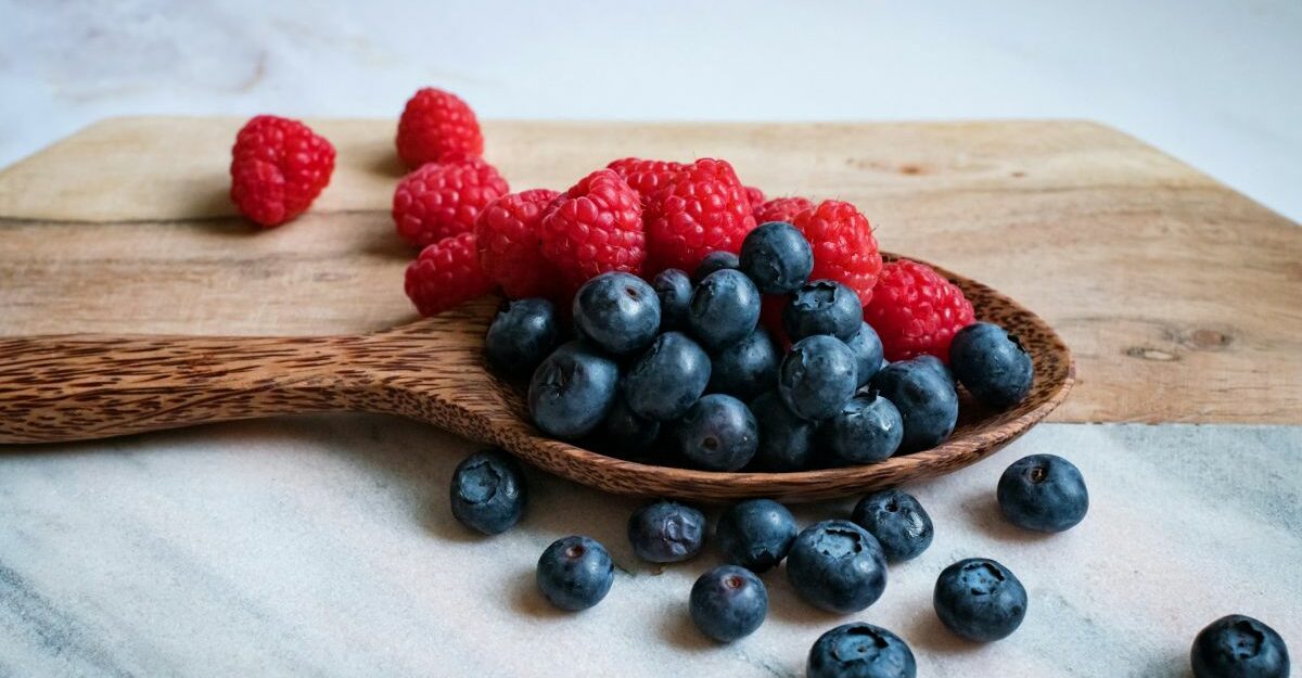 Raspberries and blueberries spread out on wooden cutting board.