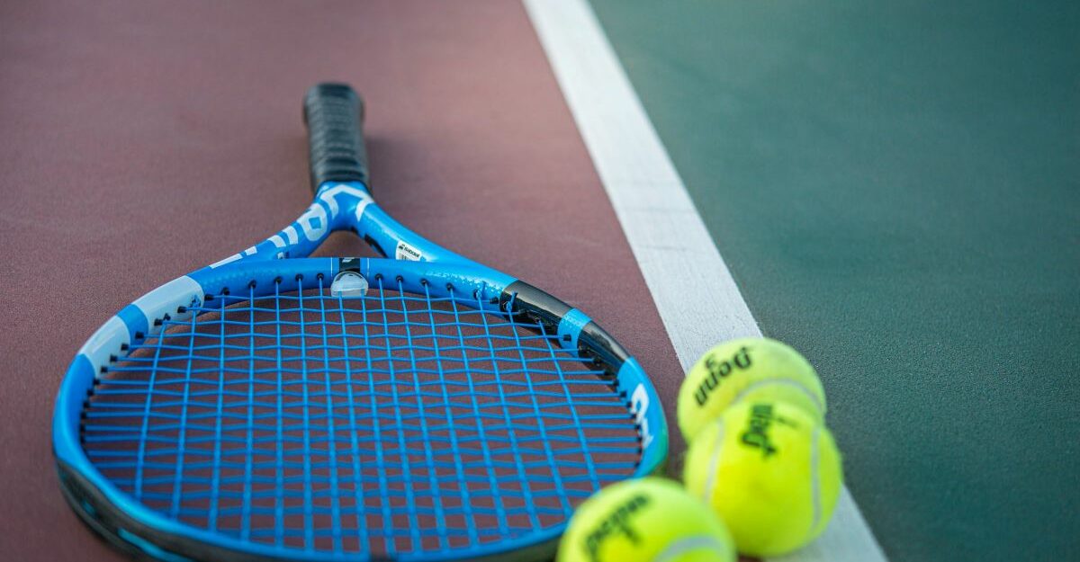 A racquet sits next to three neon green balls on a tennis court.