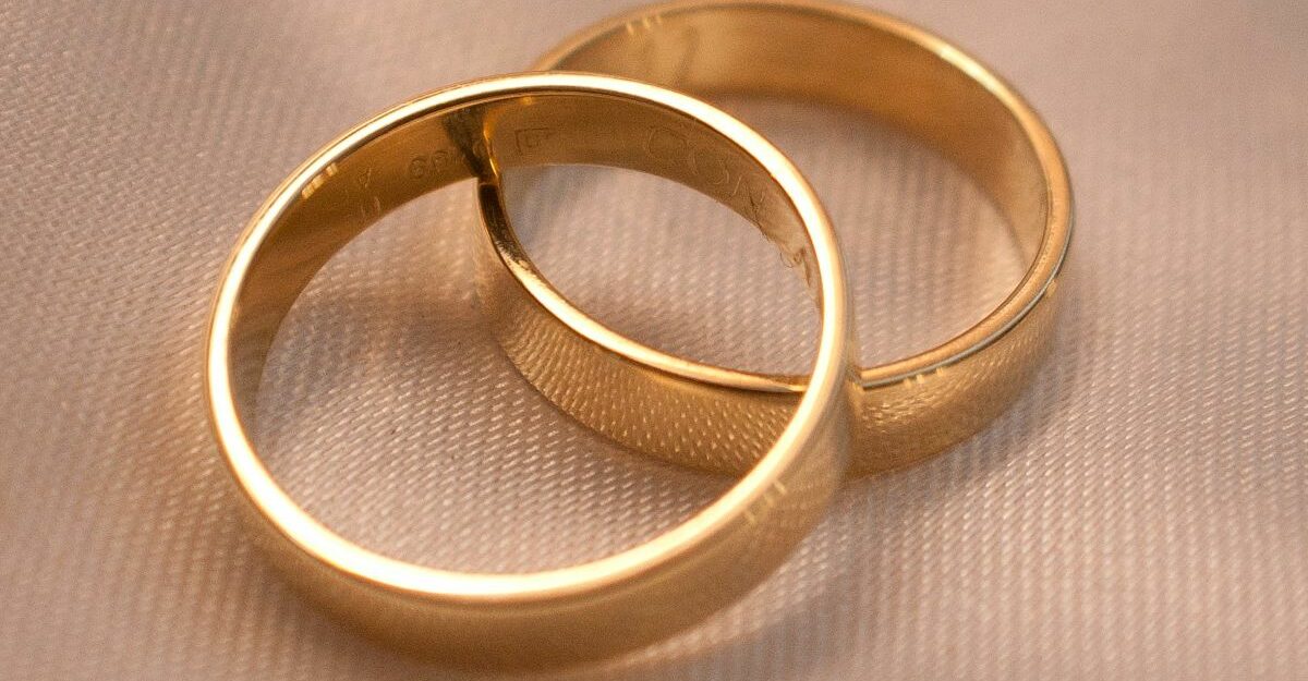 A pair of gold rings lean against each other on light pink fabric.