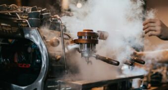 A photo of a coffee machine with steam rising from it. (Photo: Krists Luhaers / Unsplash)