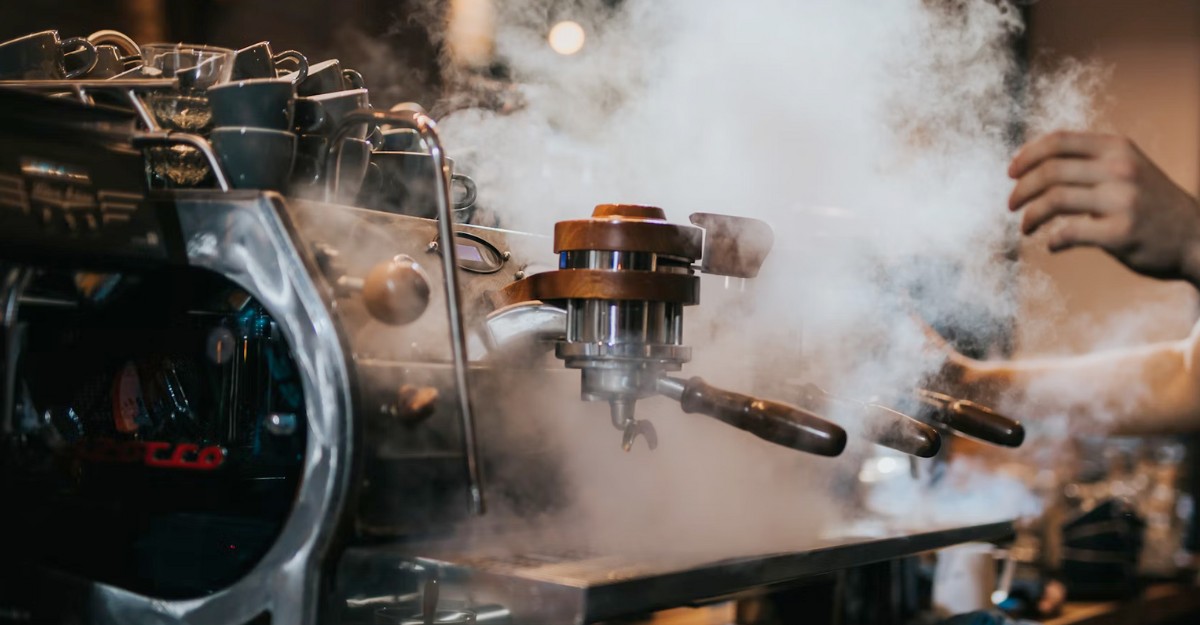 A photo of a coffee machine with steam rising from it. (Photo: Krists Luhaers / Unsplash)