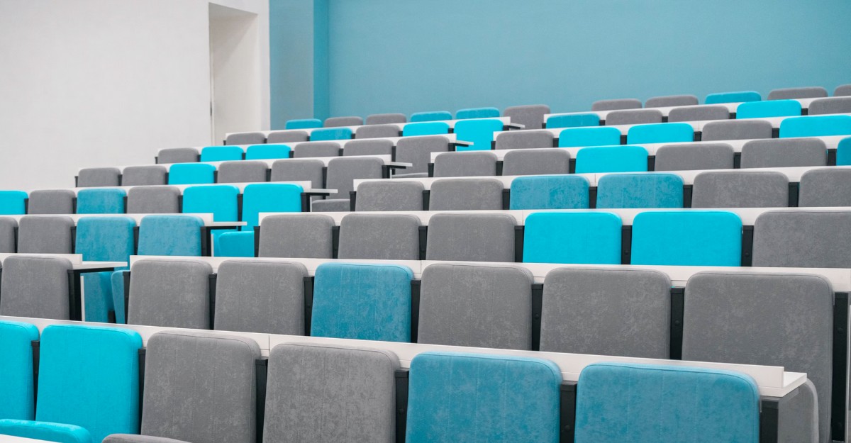 A lecture hall with grey and blue chairs. (Photo: rutmiit / Unsplash)