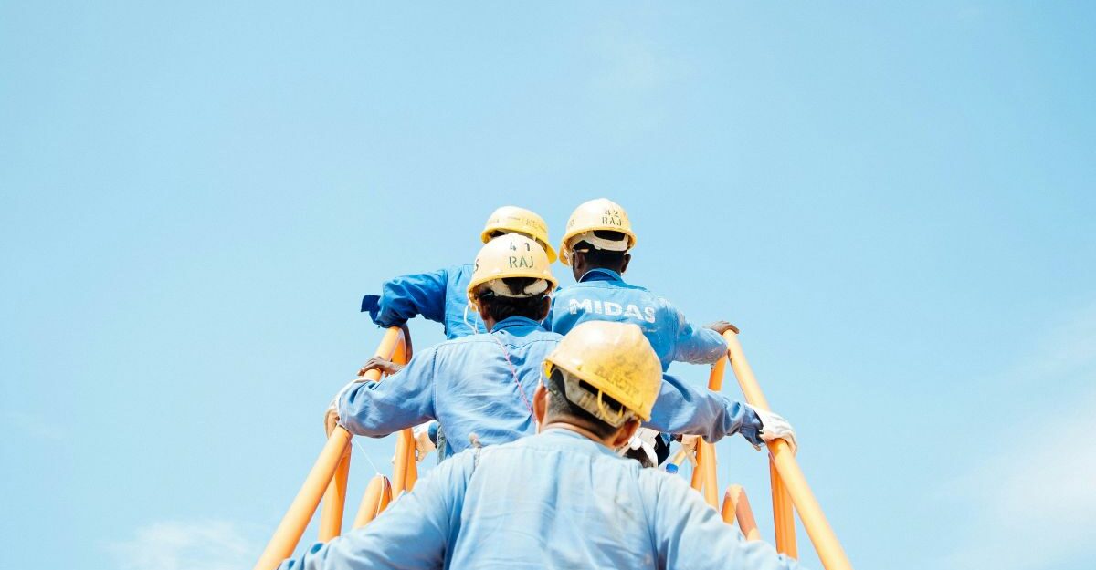 A group of construction workers in blue uniforms and yellow helmets climbing scaffolding under a clear blue sky, symbolizing dependent contractors in Ontario who rely on one main company for work.