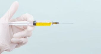 A person holds a syringe with a yellow fluid inside. (Photo: diana_pole / Unsplash)