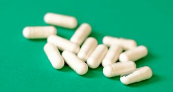 White pills on a green table. (Photo: Daniel Dan / Unsplash)