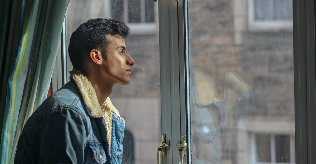 A person looks out a window. (Photo: Abdullah Ali / Unsplash)