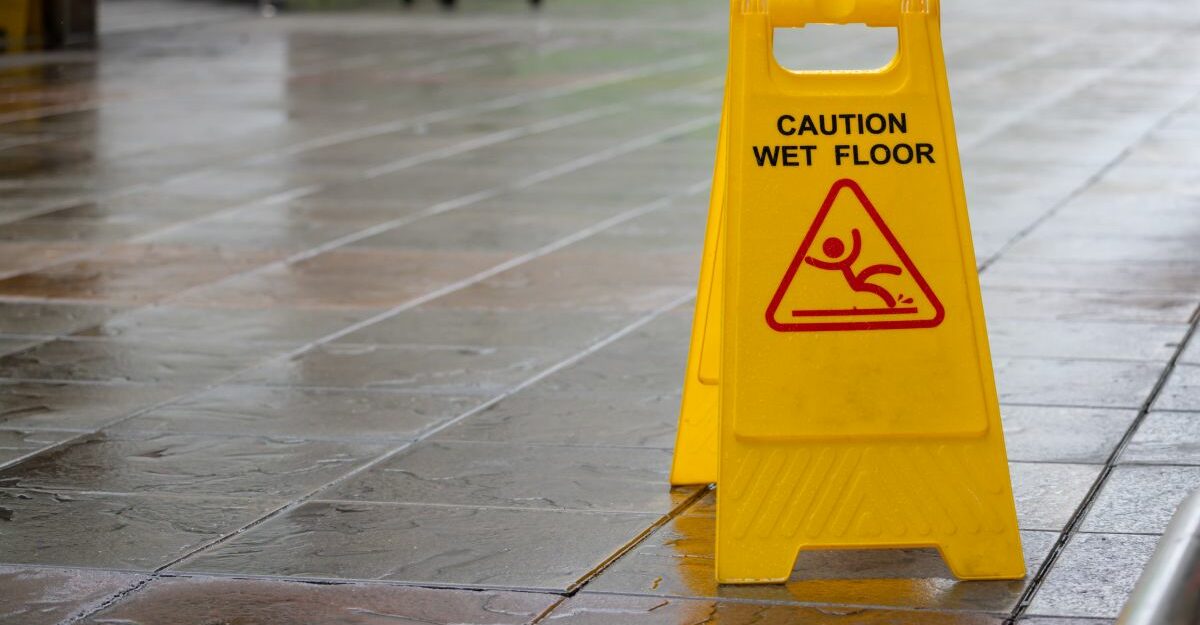 Yellow “Caution Wet Floor” sign placed on a wet tile walkway, indicating a slipping hazard in a public area.