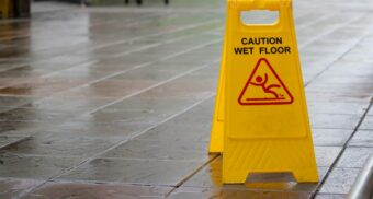 Yellow “Caution Wet Floor” sign placed on a wet tile walkway, indicating a slipping hazard in a public area.