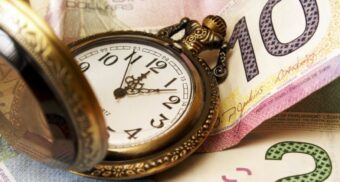A clock resting on Canadian currency. (Photo: Google Images)