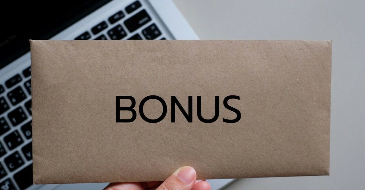 Envelope labeled “BONUS” held over a laptop keyboard, representing bonus pay in the workplace.