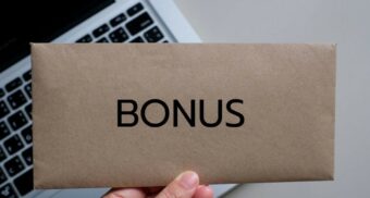 Envelope labeled “BONUS” held over a laptop keyboard, representing bonus pay in the workplace.