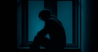 An individual sits near a window in a dark room. (Photo: Satyam Pathak / Unsplash)