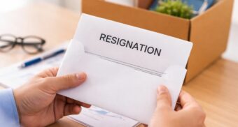 Person holding a resignation letter in an office setting with documents and personal items on desk