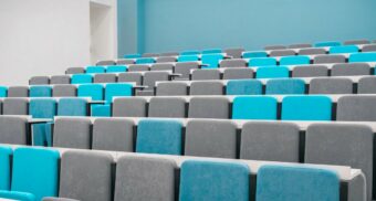 A lecture hall with blue and grey seats. (Photo: rutmiit / Unsplash)