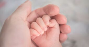 A baby's hand rests inside their parent's hand. (Photo: Hu Chen / Unsplash)