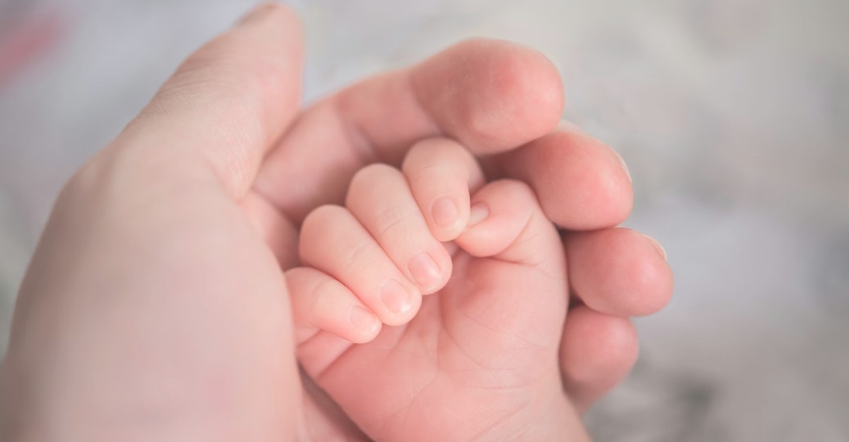 A baby's hand rests inside their parent's hand. (Photo: Hu Chen / Unsplash)